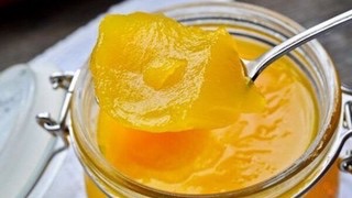 Łyżka unosi gęsty żółty przetwór ze szklanego słoika